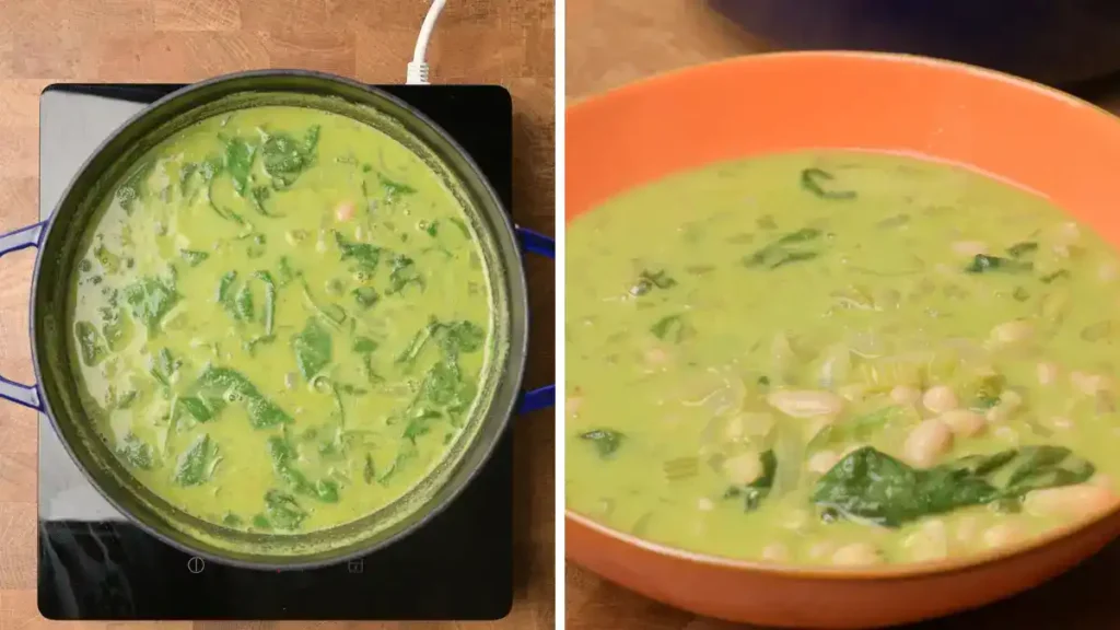 A bowl of vibrant green curry soup, centrally positioned in the image. The soup is filled with various vegetables, including diced zucchini, sweet potatoes, green beans, and white beans. Small pieces of onion are also visible. The soup's vibrant green color comes from herbs and spices, creating a rich, savory visual. The soup is thick and appears creamy, with visible pieces of vegetables throughout. The bowl is white, and the wooden table underneath is a dark brown. The lighting is even, highlighting the colors of the soup and vegetables, and casting no strong shadows. The perspective is directly overhead, looking down into the bowl. The composition is focused on showcasing the soup's contents in detail. The overall atmosphere is warm and inviting, suggesting a healthy and delicious meal.
