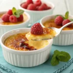 Three ramekins of crème brûlée garnished with fresh raspberries and mint leaves